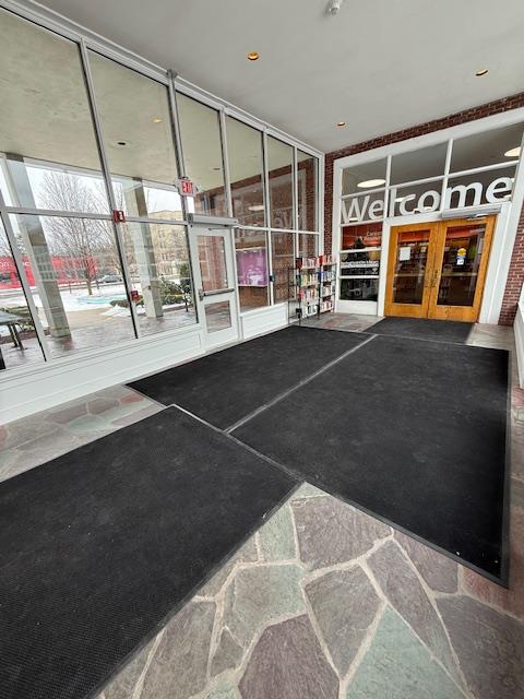 The doors into the library through the atrium. The floor is multicolored stone, covered with non-slip mats. There is a large sign over the library door that says "Welcome."